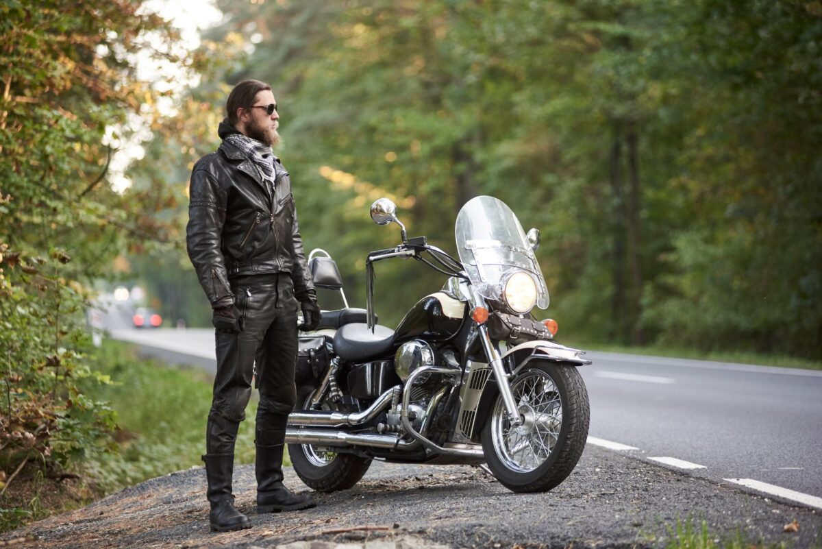Motorradfahrer mit Lederoutfit und Maschine am Waldrand